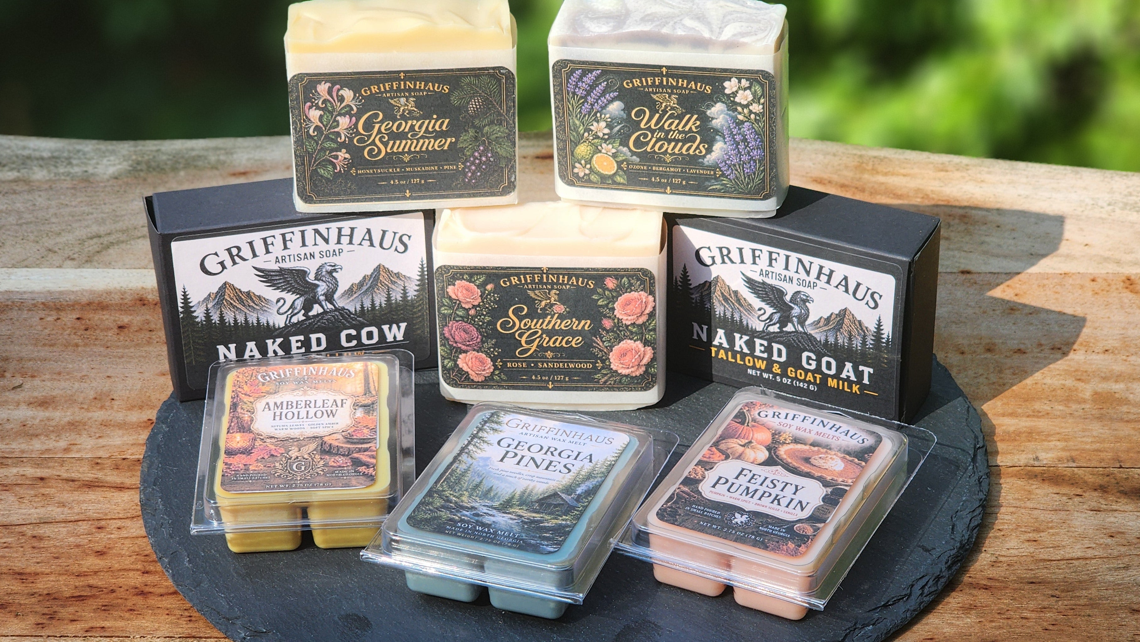 A collection of Griffinhaus scented wax melts in various colors and flavors, arranged on a black slate tray on a rustic wooden table with a blurred green garden background.