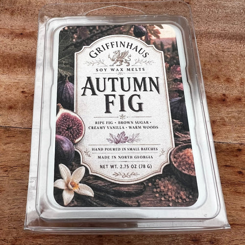 Griffinhaus Autumn Fig soy wax melts in a clear plastic clamshell package, placed on a wooden surface. The label features illustrations of ripe figs, a white flower, and warm wood textures.