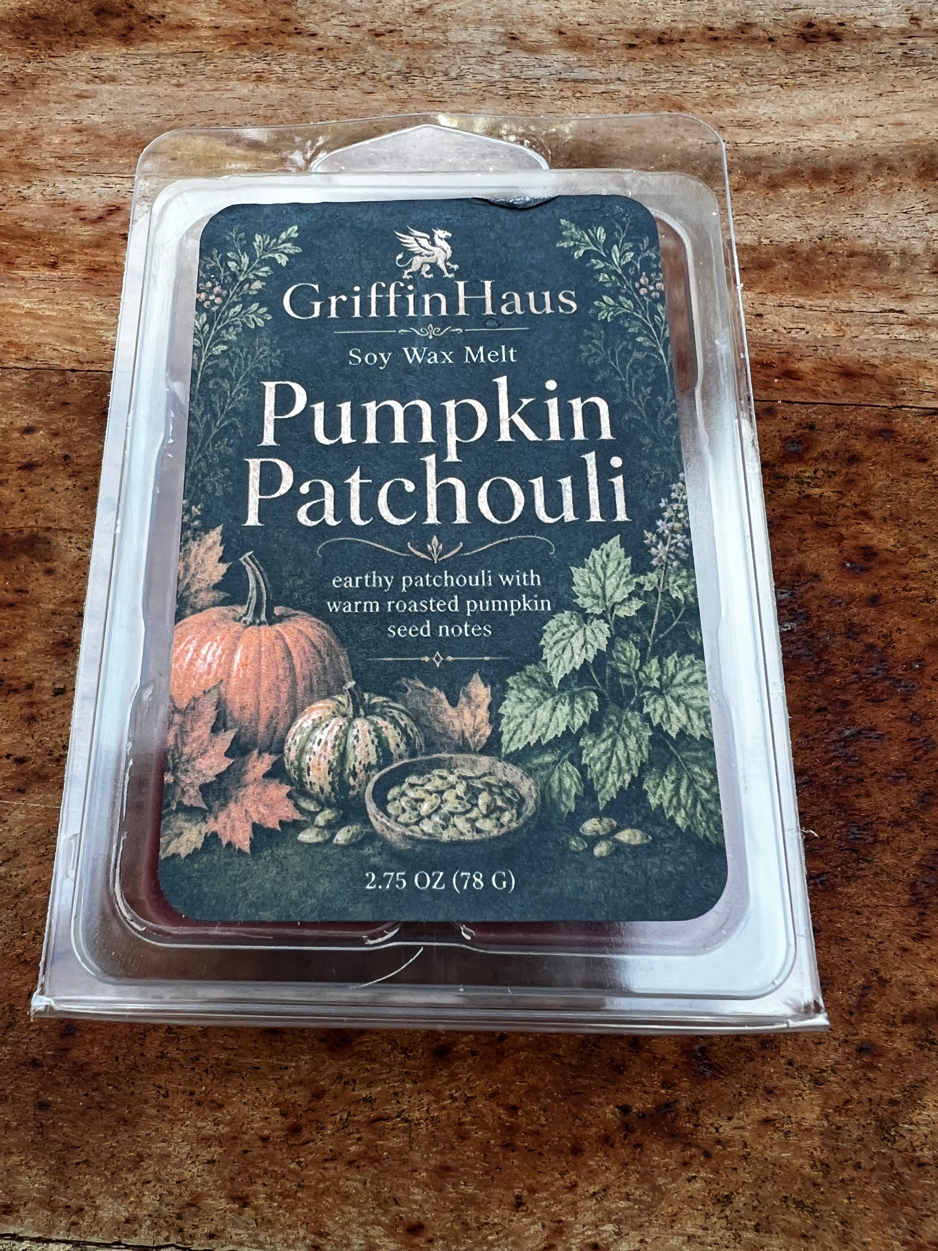 GriffinHaus Pumpkin Patchouli soy wax melt in a clear plastic clamshell package, placed on a wooden surface. The label features a dark teal background with illustrations of pumpkins, leaves, and a bowl of seeds.