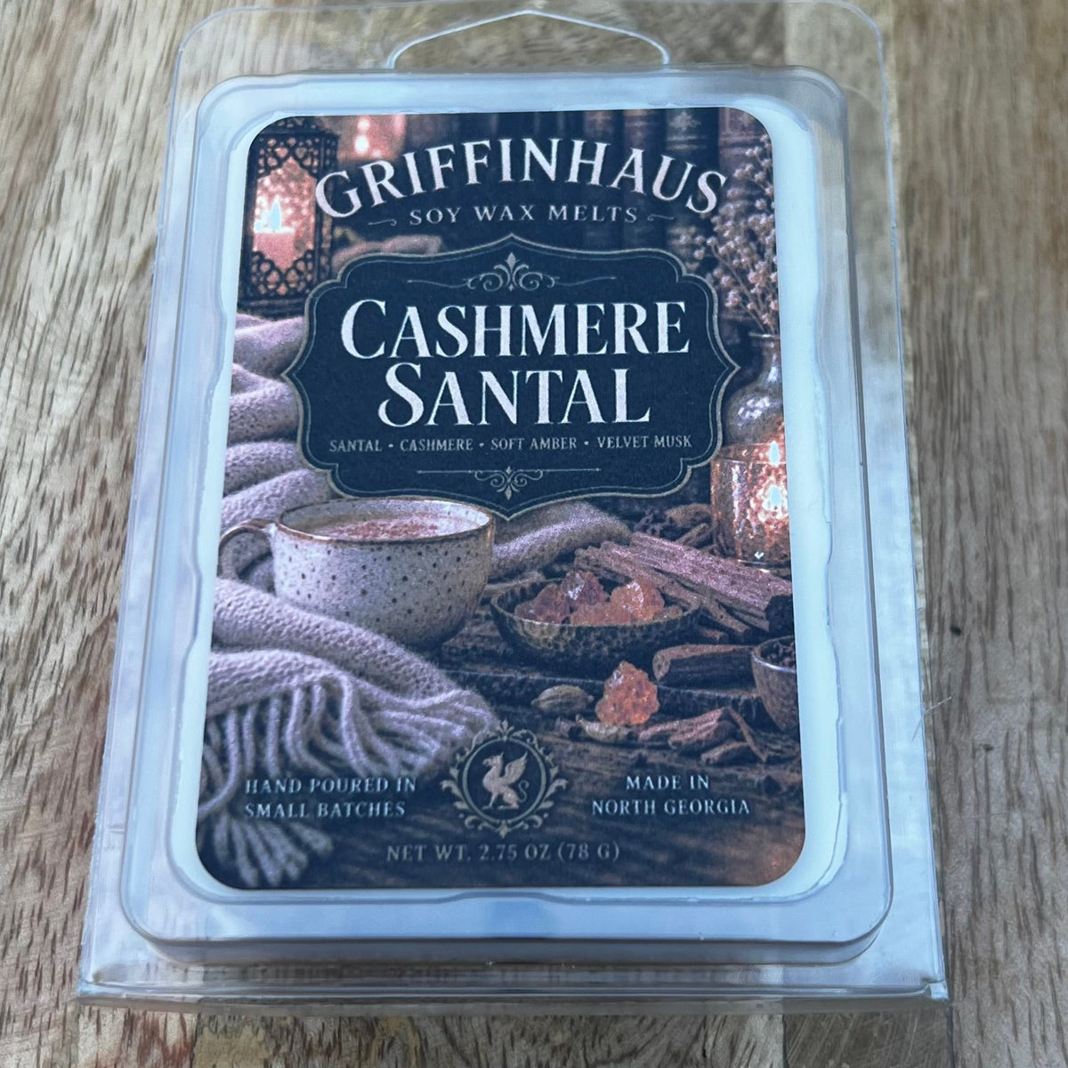 Griffinhaus Cashmere Santal scented wax melts in a clear plastic clamshell package, placed on a rustic wooden surface.