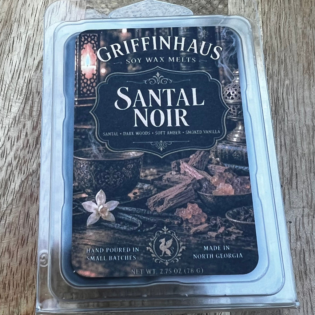 Griffinhaus Santal Noir scented soy wax melts in a clear clamshell package, placed on a rustic wooden surface.