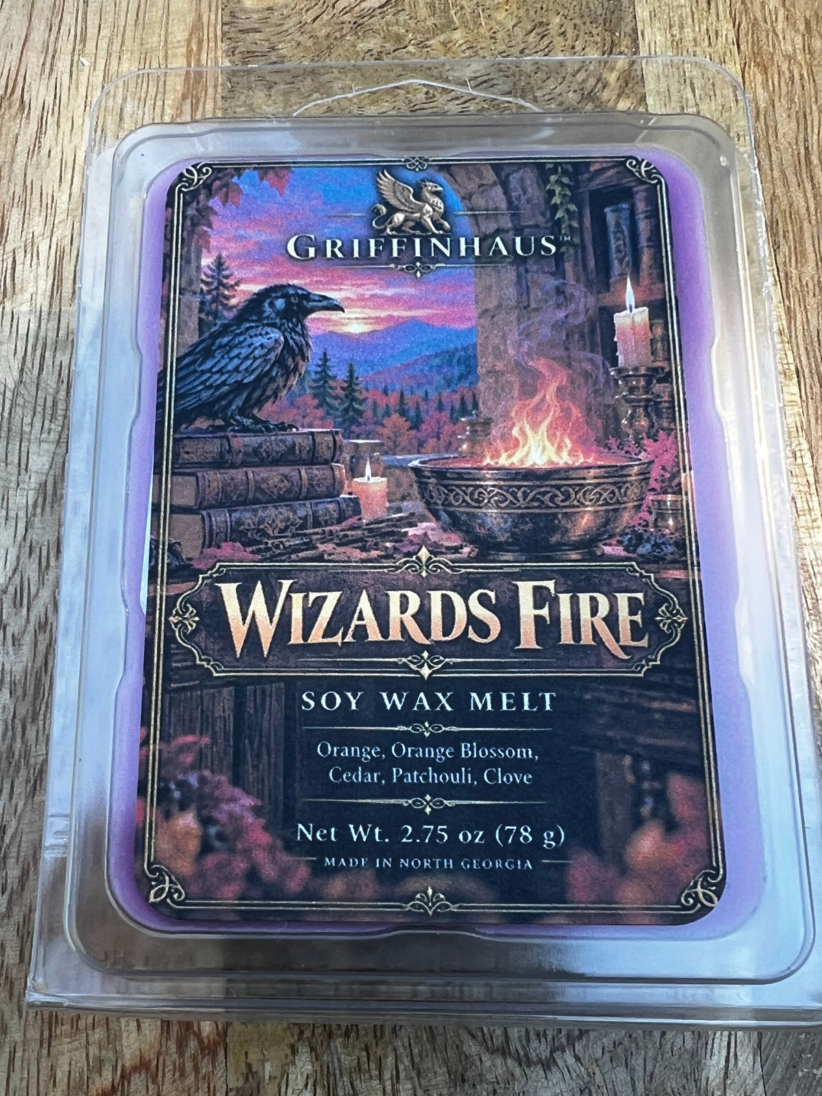 A boxed card game product labeled 'Wizards Fire' and 'Grimbound' placed on a wooden tabletop. The item is sealed in a clear plastic clamshell package, with a dark illustrated front showing a wizard-themed scene in purple, pink, blue, and black tones.